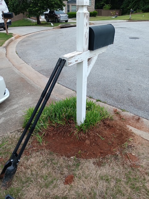 Weathered white mailbox post leaning next to a dug-up flower bed, before the project
