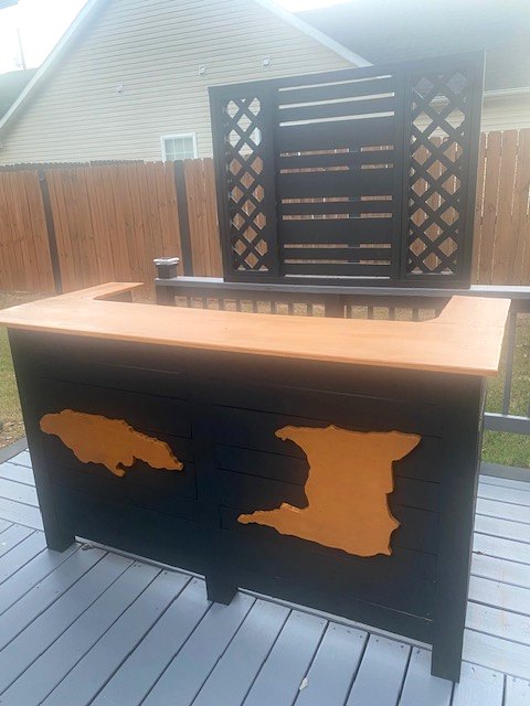 A black outdoor bar with a natural wood top, lattice back panels, and orange island silhouettes
