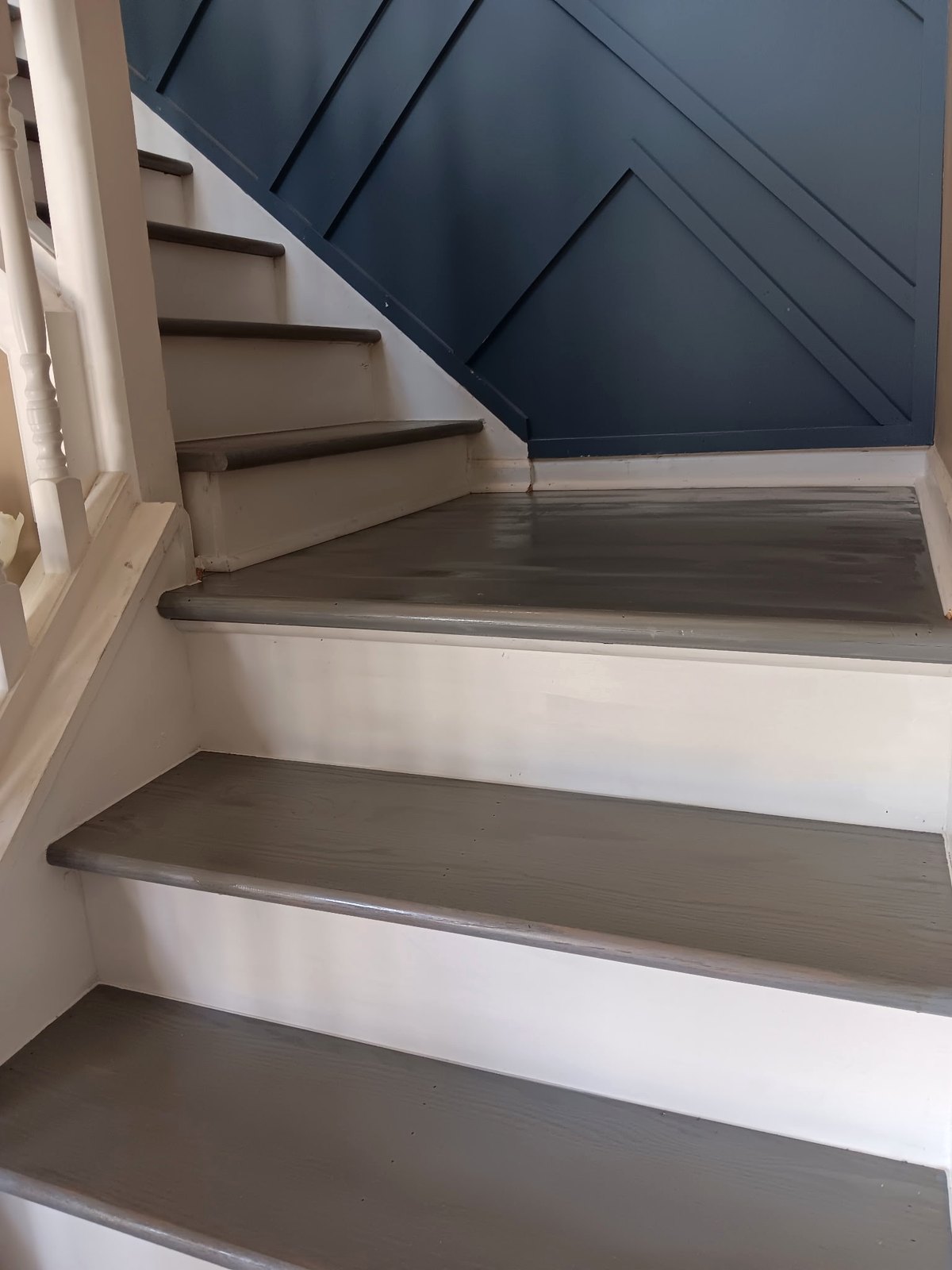 Refinished staircase with gray treads beside a dark blue paneled wall