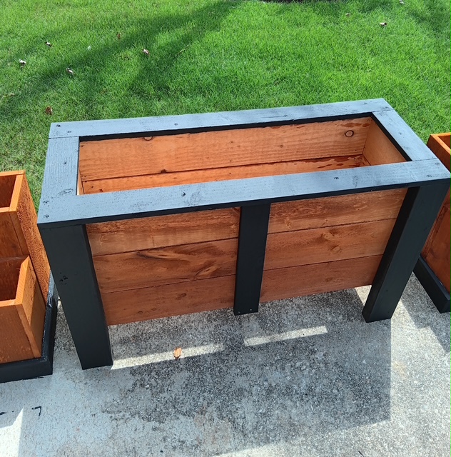Raised wooden planter box with a warm stained finish and contrasting dark trim