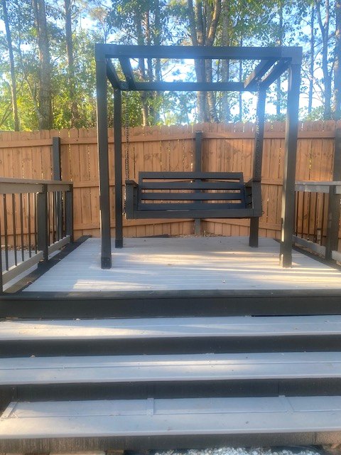 A custom wooden porch swing and matching frame on a low deck in a fenced backyard