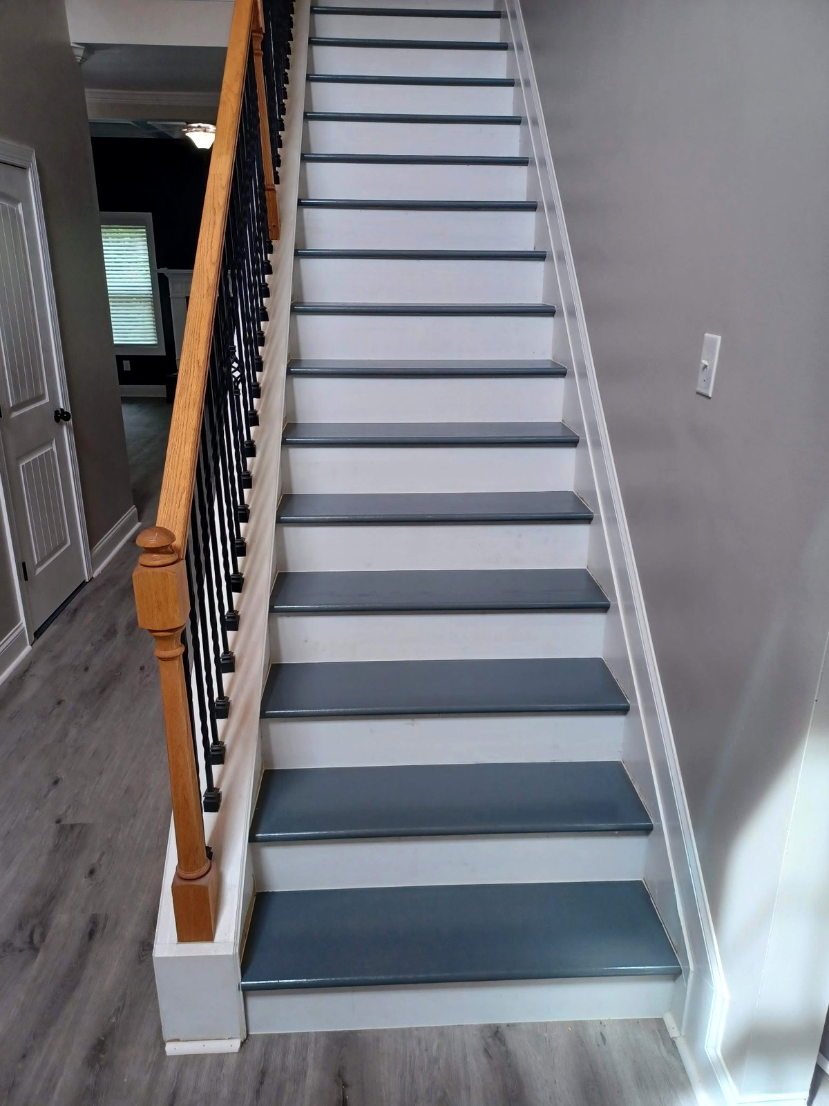 A finished staircase with dark gray treads and white risers beside a wooden handrail